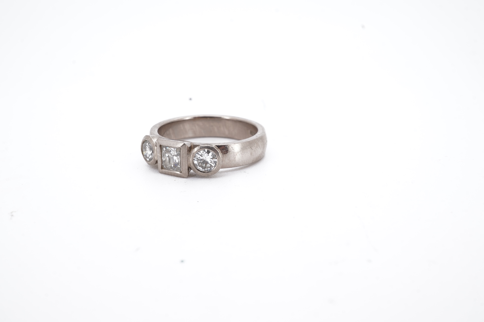 A modern 18ct white gold and three stone diamond ring, set with single square cut diamond and two round cut diamonds, size K, gross weight 5.8 grams.